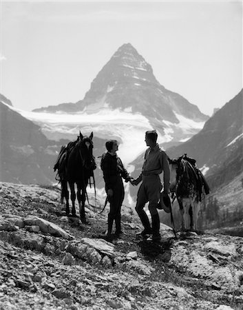 simsearch:846-02793156,k - 1930ER JAHREN PAAR MANN FRAU HAND IN HAND STEHEND MIT PFERDEN IN BERGEN WESTLICHEN MOUNT ASSINIBOINE KANADA Stockbilder - Lizenzpflichtiges, Bildnummer: 846-02796692