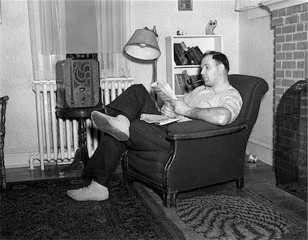 1950s MAN SITTING IN CHAIR IN LIVING ROOM SMOKING PIPE READING PAPER LISTENING TO RADIO Foto de stock - Con derechos protegidos, Código: 846-02796719