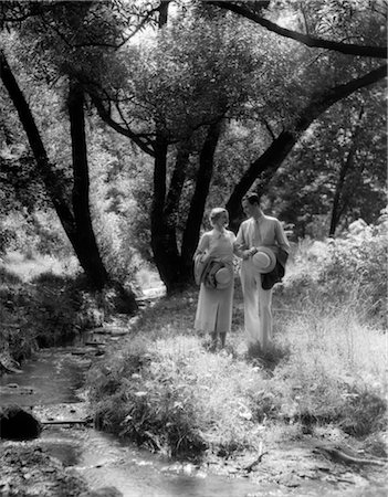 simsearch:846-02793805,k - 1930s MAN & WOMAN WALKING ALONG CREEK IN WOODS CARRYING HATS & TALKING Stock Photo - Rights-Managed, Code: 846-02796750