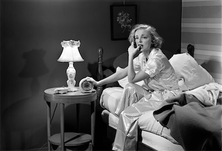 1950s WOMAN SILK PAJAMAS SITTING EDGE OF BED STRESSED SERIOUS WORRIED SLEEPLESS HOLDING ALARM CLOCK NIGHT TABLE LAMP INSOMNIA Stock Photo - Rights-Managed, Code: 846-02796777