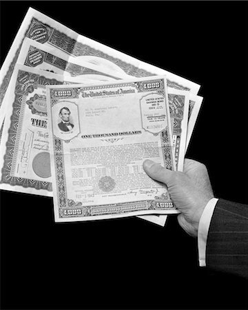 1940s MANS HAND HOLDING 4 STOCKS BONDS CERTIFICATES DOCUMENTS VALUE 1000 DOLLARS FINANCE STOCK SAVINGS BOND BANKING WEALTH Fotografie stock - Rights-Managed, Codice: 846-02796846