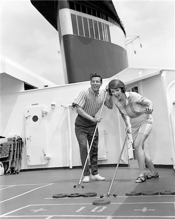 COUPLE MAN WOMAN SHIPBOARD PLAY PLAYING SHUFFLE BOARD ABOARD SHIP EXPRESSION FUN HAPPY VACATION SUMMER 1960s Stock Photo - Rights-Managed, Code: 846-02796941