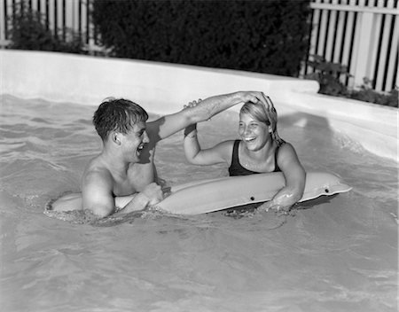 people floating swimming pools - ANNÉES 1960 TEEN COUPLE IN PISCINE FLOTTANTE SUR RADEAU MÂLE METTANT LA MAIN SUR LA TÊTE DE LA FEMELLE À DUNK LUI Photographie de stock - Rights-Managed, Code: 846-02797001