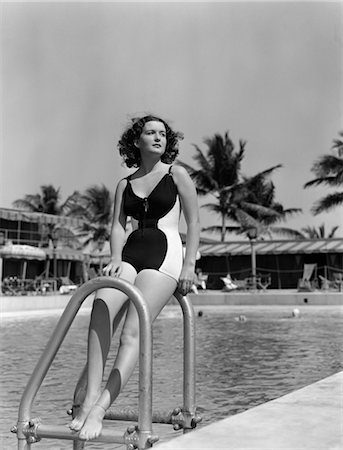 1940s BRUNETTE BATHING BEAUTY LEANING ON SWIMMING POOL LADDER WITH MOTEL & PALM TREES IN BACKGROUND Foto de stock - Con derechos protegidos, Código: 846-02797035