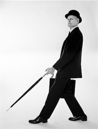 1970s SIDE VIEW OF SALESMAN IN SUIT & BOWLER WITH BRIEFCASE STEPPING FORWARD HOLDING UMBRELLA OUT IN FRONT OF HIM Foto de stock - Con derechos protegidos, Código: 846-02797042