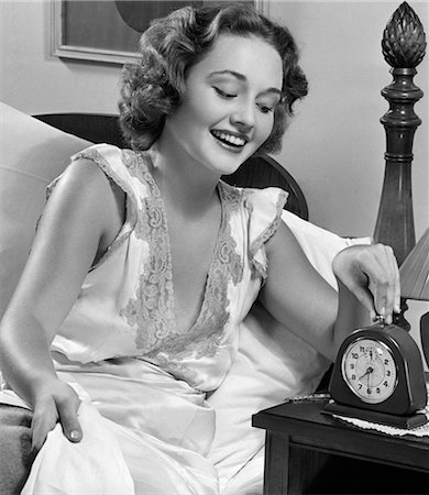 ANNÉES 1950 FEMME SOURIANTE AU LIT RÉGLAGE ALARM CLOCK Photographie de stock - Rights-Managed, Code: 846-02797142
