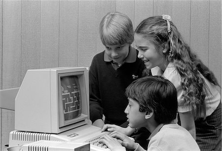simsearch:846-02797198,k - 1980s BOY SITTING IN FRONT OF COMPUTER PLAYING GAMES BOY & GIRL LOOKING ON OVER HIS SHOULDER Stock Photo - Rights-Managed, Code: 846-02797168