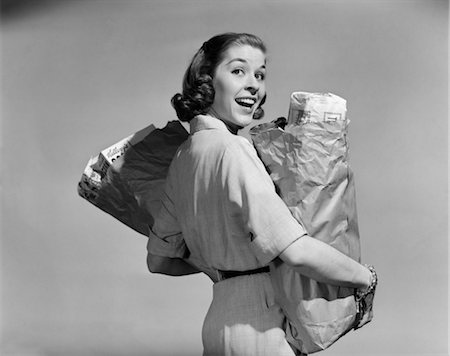 1950s SMILING WOMAN CARRYING GROCERY BAGS BOTH HANDS LOOKING BACK OVER SHOULDER Stock Photo - Rights-Managed, Code: 846-02797195