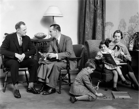 father and son black and white - 1930s FAMILY IN LIVING ROOM MOTHER KNITS DAUGHTER ON HER LAP WITH BOOK SON ON FLOOR WITH HAMMER Stock Photo - Rights-Managed, Code: 846-02797349