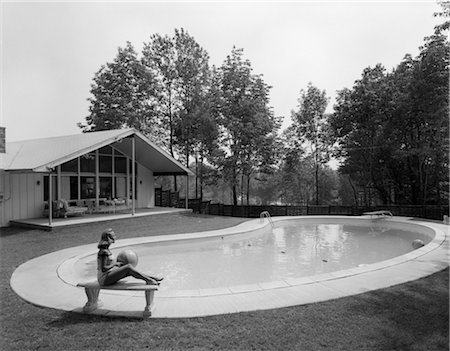 swimming pool people b&w - 1960s BLOND IN BATHING SUIT SITTING ON STONE BENCH WITH BEACH BALL IN LAP NEAR KIDNEY SHAPED SWIMMING POOL IN BACKYARD Stock Photo - Rights-Managed, Code: 846-02797352
