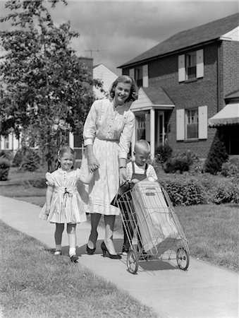 simsearch:846-02796911,k - 1950s MOTHER WALKING DOWN SUBURBAN SIDEWALK HOLDING DAUGHTER'S HAND & HELPING SON TO PUSH 2-WHEELED GROCERY CART Stock Photo - Rights-Managed, Code: 846-02797396