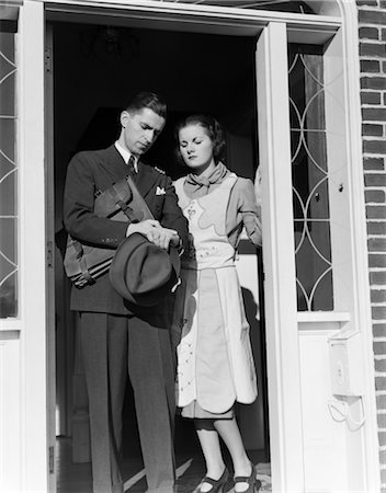 1930s HUSBAND WIFE STAND IN OPEN DOOR MAN GOING TO WORK CHECKING WATCH HOLDING BRIEFCASE HAT IN HAND Stock Photo - Rights-Managed, Code: 846-02797419