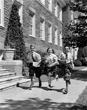 1940s GROUP OF THREE SCHOOL CHILDREN 2 BOYS 1 GIRL RUNNING DOWN SIDEWALK CARRYING BOOKS Stock Photo - Rights-Managed, Code: 846-02797552