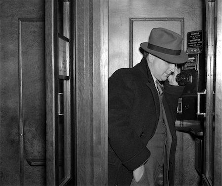 ANNÉES 1940 HOMME VÊTU D'UN COSTUME DE FEDORA ET MANTEAU DEBOUT DANS UNE CABINE TÉLÉPHONIQUE DU BOIS PRÉFINI Photographie de stock - Rights-Managed, Code: 846-02797589