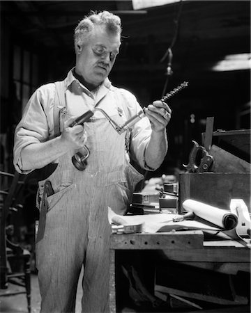 1920s OLDER MAN IN OVERALLS STANDING AT WORKBENCH HOLDING HAND DRILL Stock Photo - Rights-Managed, Code: 846-02797601