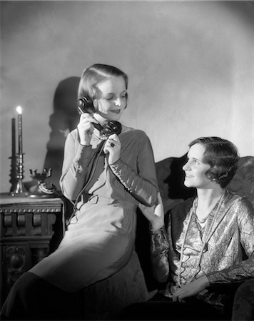 electric device woman - 1920s 1930s TWO WOMEN ONE TALKING ON PHONE OTHER SITTING IN CHAIR CANDLE LIGHT Stock Photo - Rights-Managed, Code: 846-02797636