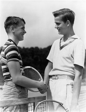 ANNÉES 1930 1940 DEUX JOUEURS DE TENNIS GARÇON SERRANT LA MAIN APRÈS UN MATCH À LA HOLDING NET RAQUETTES Photographie de stock - Rights-Managed, Code: 846-02797688