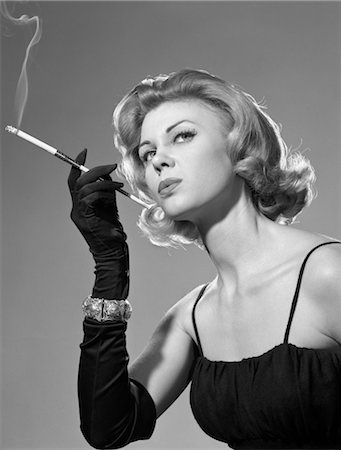 ANNÉES 1960 FEMME SENSUELLE SEXY EN NOIR ROBE GANTS NOIR BRACELET FUMER CIGARETTE EN LONG FUME-CIGARETTE Photographie de stock - Rights-Managed, Code: 846-02797704