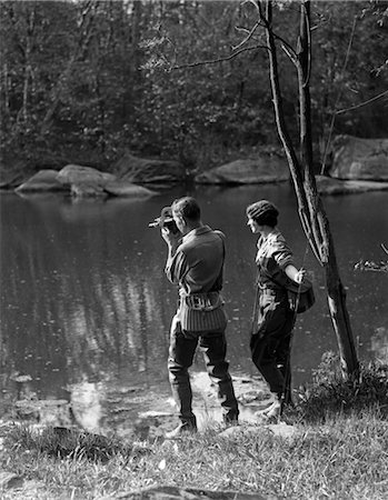 1930s MAN WITH CAMERA & WOMAN WITH TROUT ROD BOTH ARE WEARING WADERS & WICKER CREELS Stock Photo - Rights-Managed, Code: 846-02797728