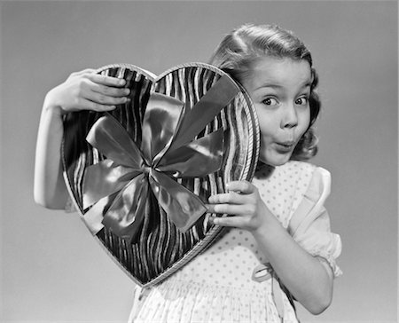 1950s SMILING GIRL PEEKING FROM BEHIND BOX OF VALENTINE CANDY HEART SHAPED BOX Stock Photo - Rights-Managed, Code: 846-02797730