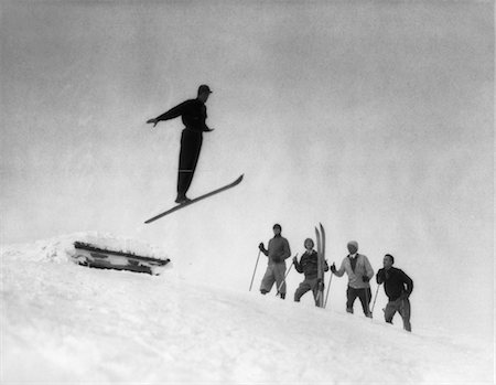 ski jumping - 1920s MEN IN SNOW WEARING WOODEN SKIS WATCHING SKI JUMPER Fotografie stock - Rights-Managed, Codice: 846-02797758