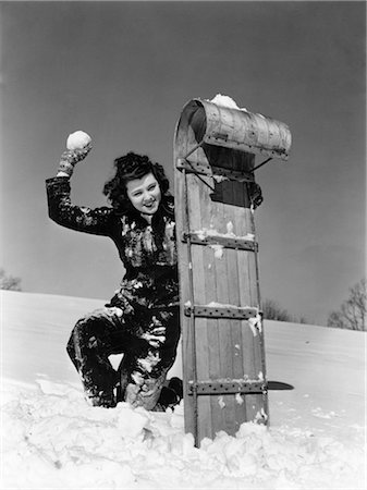 1930s WOMAN PLAYING IN SNOW HIDING BEHIND TOBOGGAN SLED HAVING A SNOWBALL FIGHT HOLDING A SNOWBALL Foto de stock - Con derechos protegidos, Código: 846-02797750