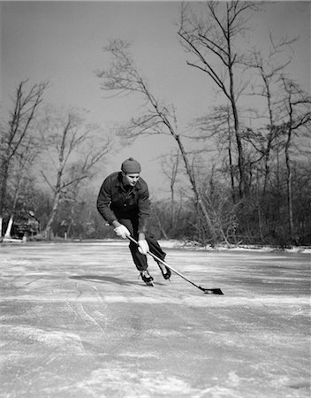 frozen ice background - 1940s MAN PLAYING ICE HOCKEY ON FROZEN LAKE CONTROLLING PUCK WITH STICK TREES IN BACKGROUND SKATE Foto de stock - Con derechos protegidos, Código: 846-02797808