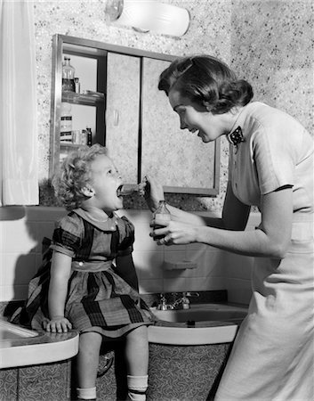 1950s MOTHER ADMINISTERING MEDICINE WITH SPOON TO YOUNG DAUGHTER WITH MOUTH WIDE OPEN SITTING ON BATHROOM SINK Stock Photo - Rights-Managed, Code: 846-02791738