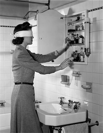 1940s WOMAN WEARING BLINDFOLD REACHING INTO BATHROOM MEDICINE CABINET Fotografie stock - Rights-Managed, Codice: 846-02791910