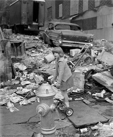 1960s GIRL STANDING ON BACK OF TRICYCLE BEHIND OPEN FIRE HYDRANT SURROUNDED BY WRECKAGE WITH OLD BEAT-UP CAR IN BACKGROUND Stock Photo - Rights-Managed, Code: 846-02792006