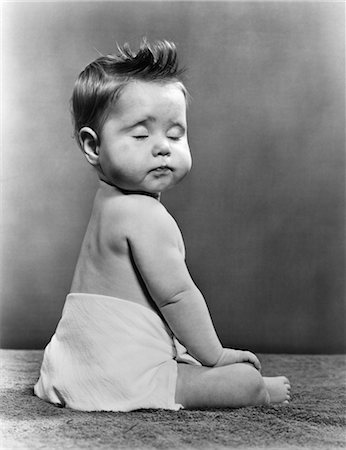 1940s 1950s BABY SEATED WITH BACK TO CAMERA TURNING HEAD TO VIEWER WITH EYES CLOSED Stock Photo - Rights-Managed, Code: 846-02792047
