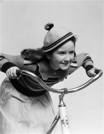 1930s SMILING EAGER LITTLE GIRL IN KNIT CAP AND MATCHING SWEATER RIDING BIKE LEANING INTO HANDLEBARS Foto de stock - Con derechos protegidos, Código: 846-02792068