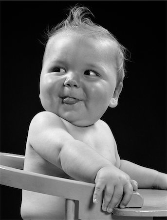 photograph 1940 - 1940s BABY IN HIGH CHAIR HEAD TURNED TO ONE SIDE WITH TONGUE STICKING OUT SILLY HAPPY FUNNY EXPRESSION Stock Photo - Rights-Managed, Code: 846-02792078