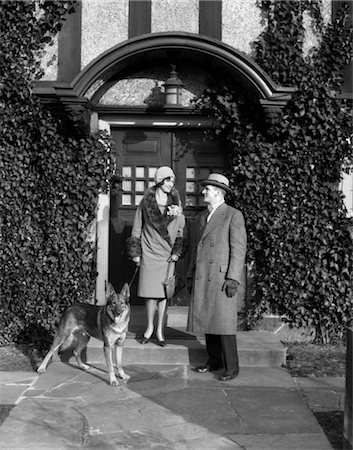 simsearch:846-02797348,k - COUPLE DES ANNÉES 1920 PORTE MANTEAU CHAPEAU GANTS ON ÉTAPES IVY COUVERTS BÂTIMENT AVEC CHIEN DE BERGER ALLEMAND SUR UNE LAISSE Photographie de stock - Rights-Managed, Code: 846-02792080