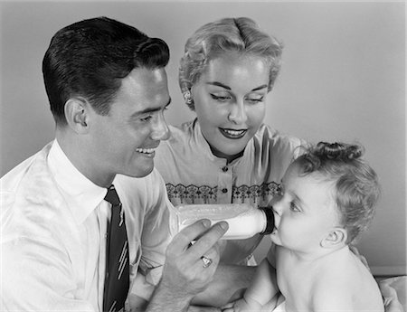 1950s SMILING FATHER FEEDING BABY MILK FROM BOTTLE WITH MOTHER AT SIDE Stock Photo - Rights-Managed, Code: 846-02792123