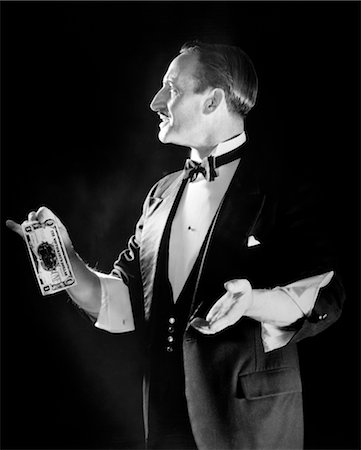 1920s MAGICIAN IN TUXEDO WITH SLEEVES ROLLED UP HOLDING OUT DOLLAR BILL Stock Photo - Rights-Managed, Code: 846-02792253