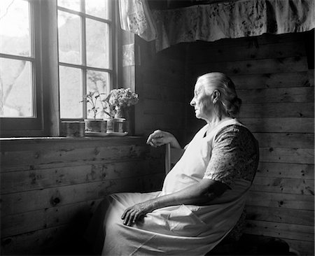 1950s ELDERLY WOMAN SEATED IN DIMLY LIT FARMHOUSE WITH PLANTS ON WINDOWSILL LOOKING OUT WINDOW WITH SUNLIGHT SHINING THROUGH Stock Photo - Rights-Managed, Code: 846-02792268