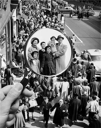 1950s MONTAGE OF FAMILY IN MAGNIFYING GLASS SUPERIMPOSED OVER CROWDED SIDEWALK Fotografie stock - Rights-Managed, Codice: 846-02792270