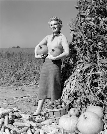 1950s 1960s WOMAN STANDING BY CORN SHOCK HOLDING A PUMPKIN UNDER EACH ARM Foto de stock - Con derechos protegidos, Código: 846-02792284