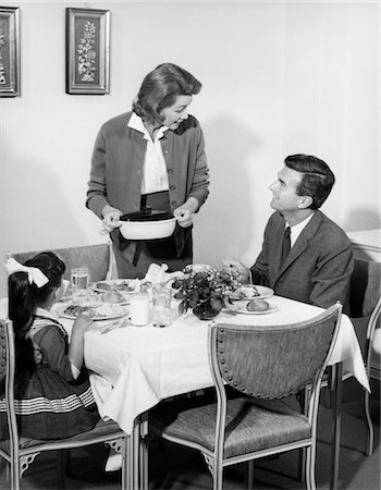 simsearch:846-02795061,k - FAMILLE DES ANNÉES 1960 DES TROIS AT TABLE DE SALLE À MANGER AU DÎNER PARLER AVEC FEMME DEBOUT METTANT COCOTTE PLAT SUR TABLE Photographie de stock - Rights-Managed, Code: 846-02792343