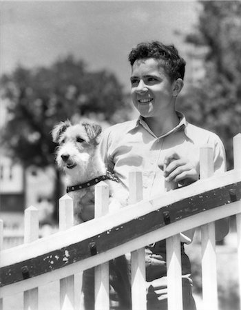 simsearch:846-03163283,k - ANNÉES 1930 TEEN BOY SOURIRE PERMANENT PAR UNE CLÔTURE HOLDING WIRE HAIRED TERRIER DOG Photographie de stock - Rights-Managed, Code: 846-02792397