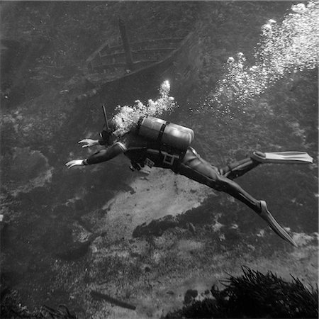 ANNÉES 1960 PLONGEUR SOUS-MARIN NAGE DANS DES BULLES DE COMBINAISON DE PLONGÉE ET PALMES EN TANT QUE PARTENT LES RÉSERVOIRS D'OXYGÈNE Photographie de stock - Rights-Managed, Code: 846-02792420