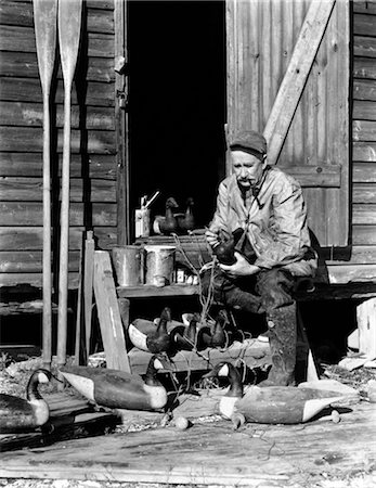 pato de isca - 1930s 1940s SENIOR MAN SITTING ON WOODEN STAIRS PAINTING DUCK DECOYS Foto de stock - Direito Controlado, Número: 846-02792451
