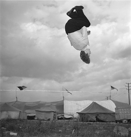 retro circus tent - 1950s MAN TIGHTROPE WALKER JUMPING THROUGH HOOP APPEARS SUSPENDED IN AIR UPSIDE DOWN Stock Photo - Rights-Managed, Code: 846-02792474