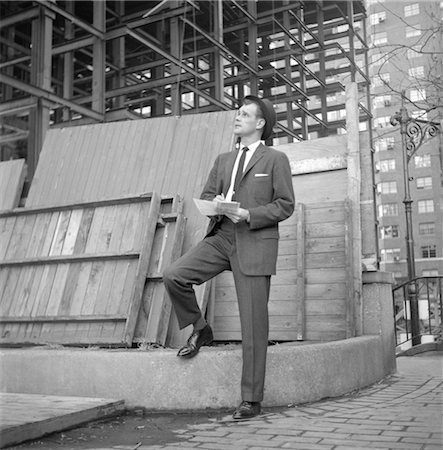 1960s BUSINESSMAN ON CURB LOOKING UP INTO BUILDING UNDER CONSTRUCTION WRITING NOTES Foto de stock - Con derechos protegidos, Código: 846-02792523