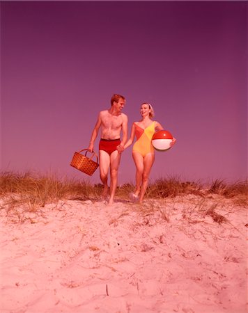 1960s COUPLE BATHING SUITS CARRYING PICNIC BASKET ON SAND DUNE Foto de stock - Con derechos protegidos, Código: 846-02792555