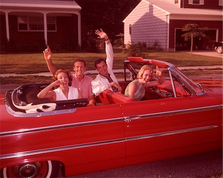 ANNÉES 1960 DEUX YOUNG TEEN COUPLE EN ROUGE DÉCAPOTABLE VOITURE DANS UNE RUE DE BANLIEUE MAINS AGITANT RIRE Photographie de stock - Rights-Managed, Code: 846-02792551