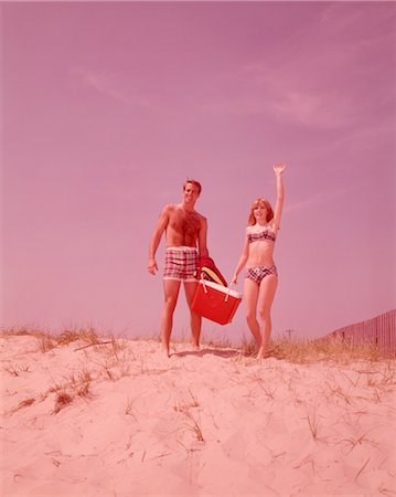 picnic on beach - ANNÉES 1960 PLAGE COUPLE MARCHANT DANS LE SABLE TRANSPORTANT REFROIDISSEUR FEMME AGITANT Photographie de stock - Rights-Managed, Code: 846-02792580