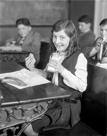 1920s SCHOOL GIRL EATING LUNCH AT HER DESK DRINKING FROM A BOTTLE OF MILK HOLDING A SANDWICH Foto de stock - Con derechos protegidos, Código: 846-02792860