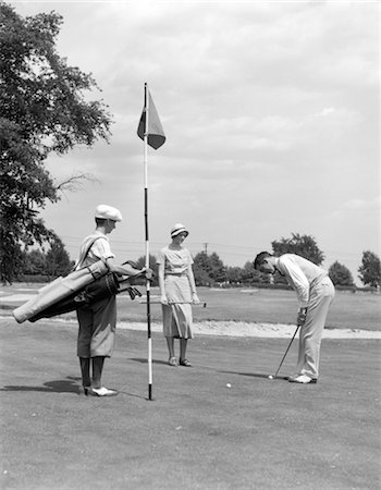 simsearch:846-02793017,k - 1930s COUPLE ON GOLF GREEN PUTTING AS THE CADDY STANDS WITH FLAG AND BAG OF CLUBS Stock Photo - Rights-Managed, Code: 846-02792944